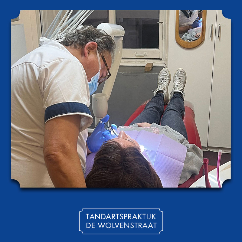 Een tandarts in een witte jas geeft een patiënt die op de behandelstoel ligt een verdoving.